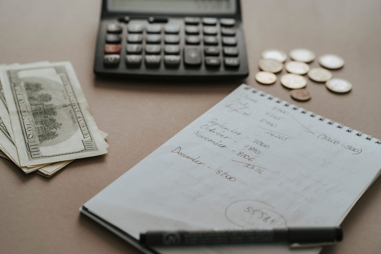 A notebook with handwritten calculations beside a pen